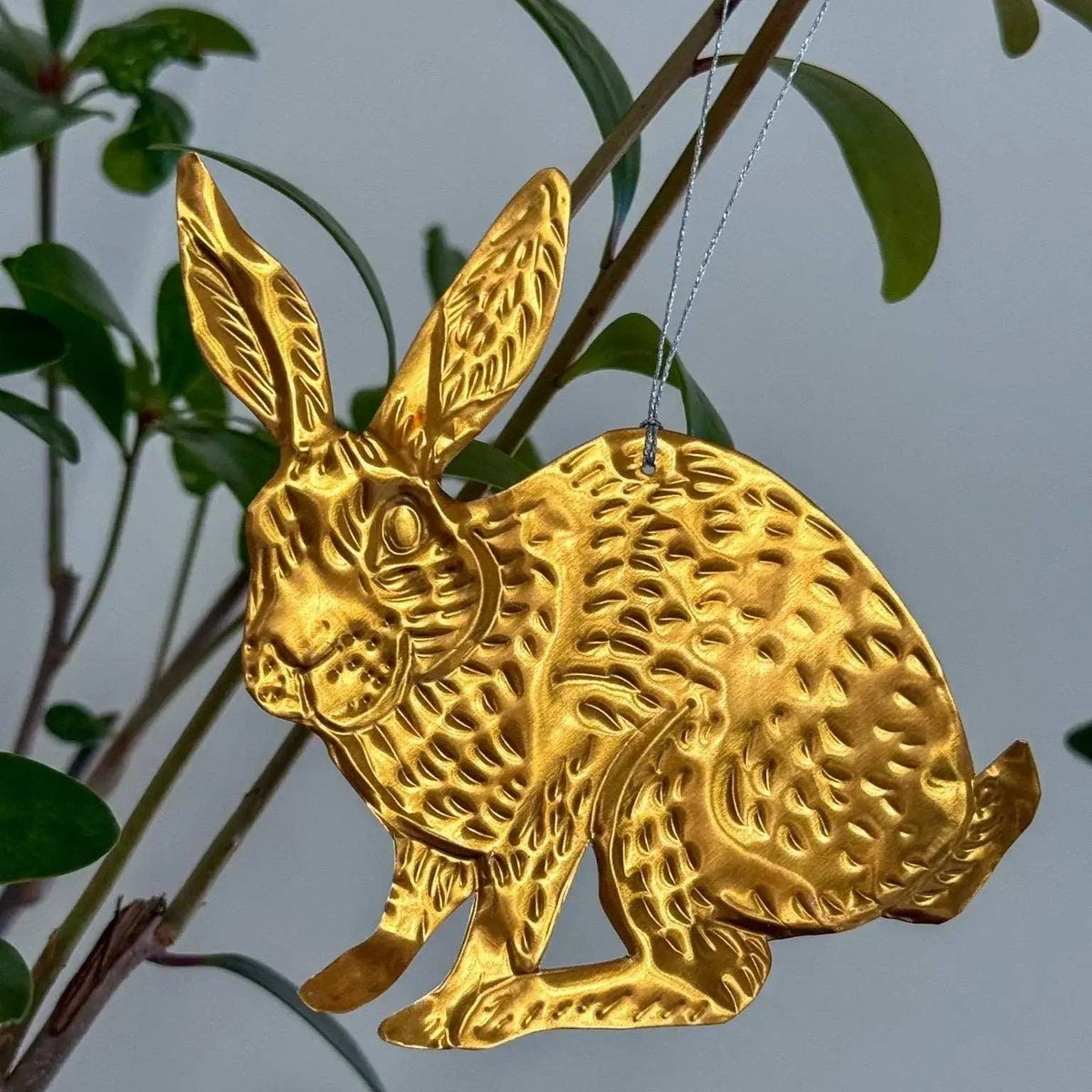Gold rabbit ornament hanging from a branch with a blurred natural background