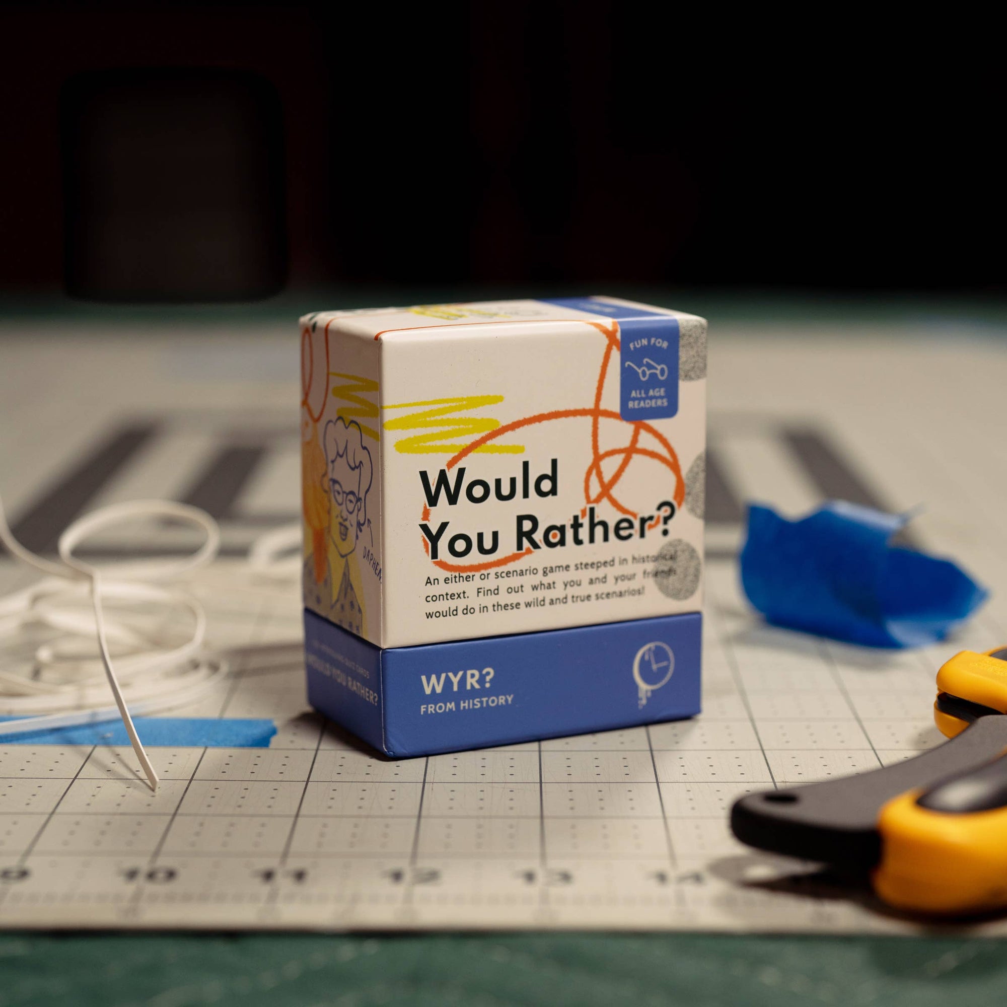 Box of 'Would You Rather?' game on a cutting mat with tools in the background