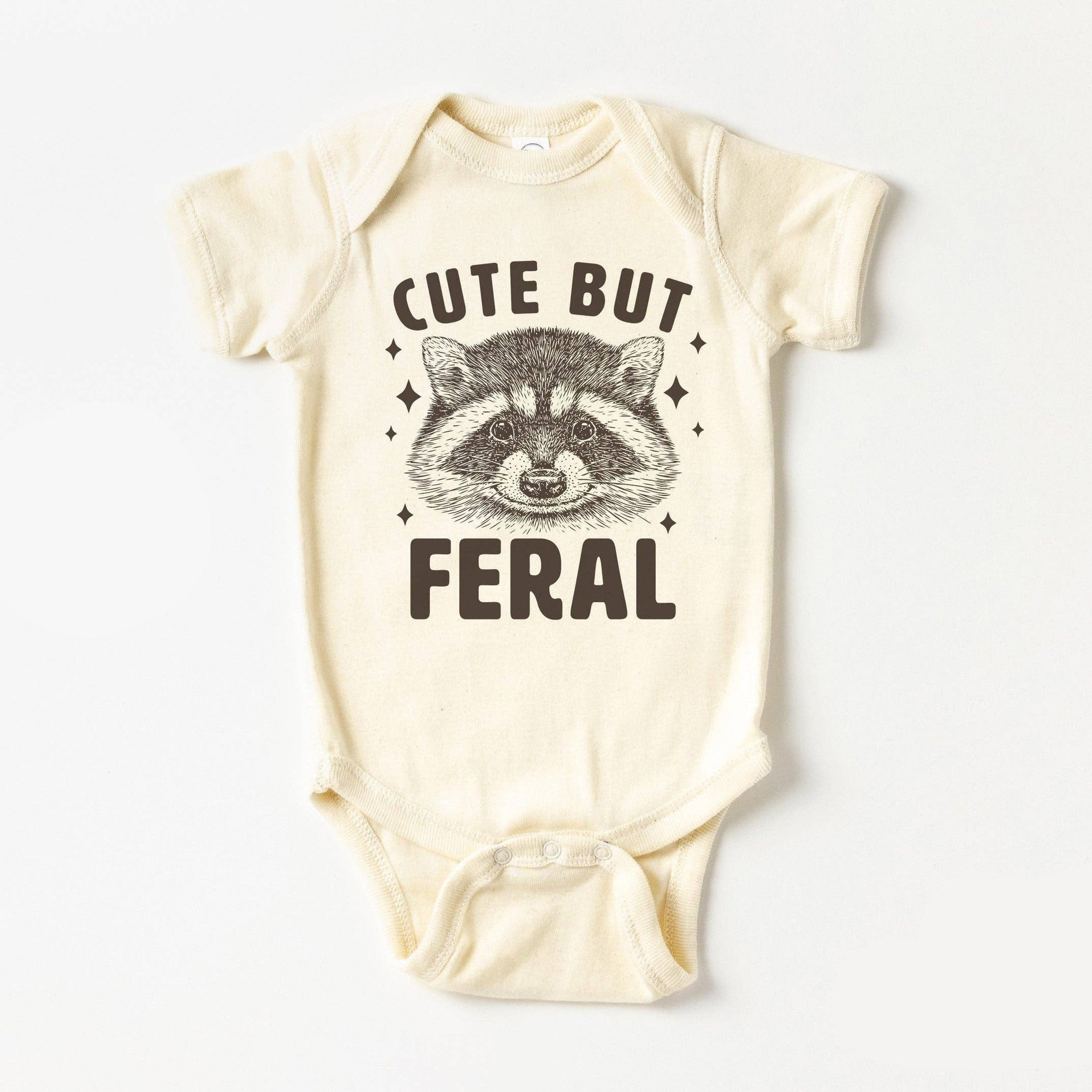 Baby onesie with raccoon graphic and text 'Cute But Feral' on a white background