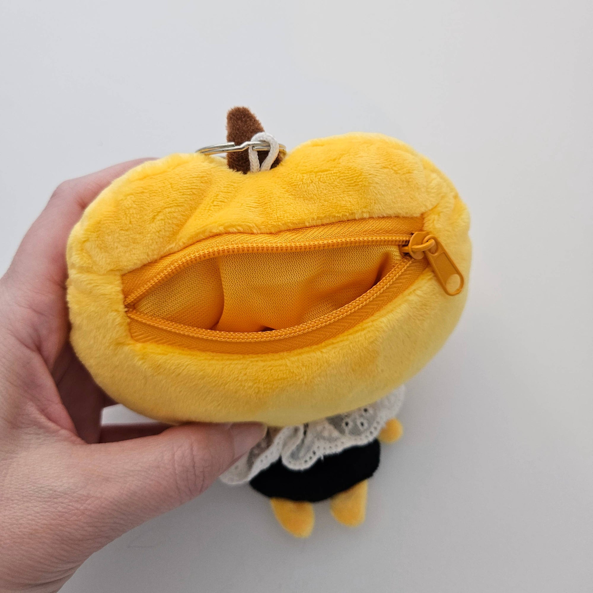 Yellow plush pumpkin-shaped coin purse held by a hand on a light gray background