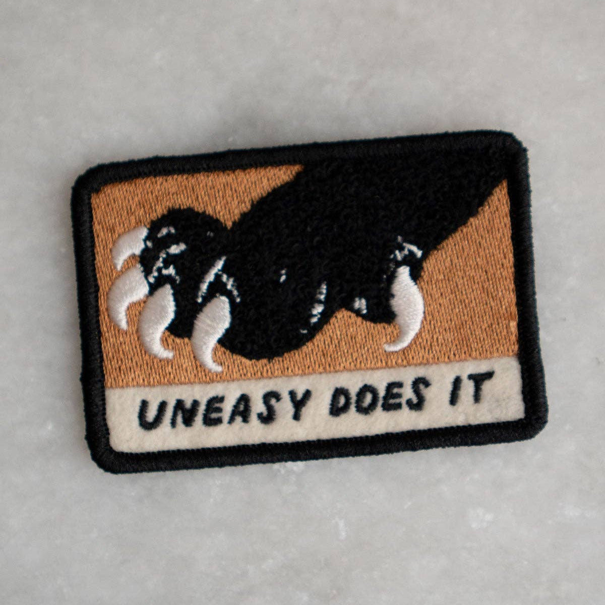 Patch with a dog illustration and 'Uneasy Does It' text on a gray background