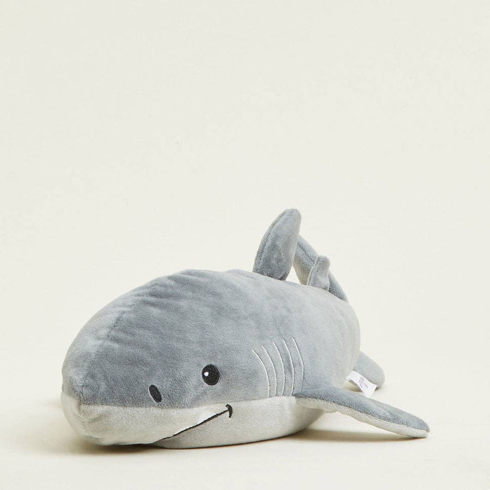 A plush shark toy in shades of gray, featuring embroidered details, a small black eye, and a tiny white tag, photographed on a clean, solid off-white background.