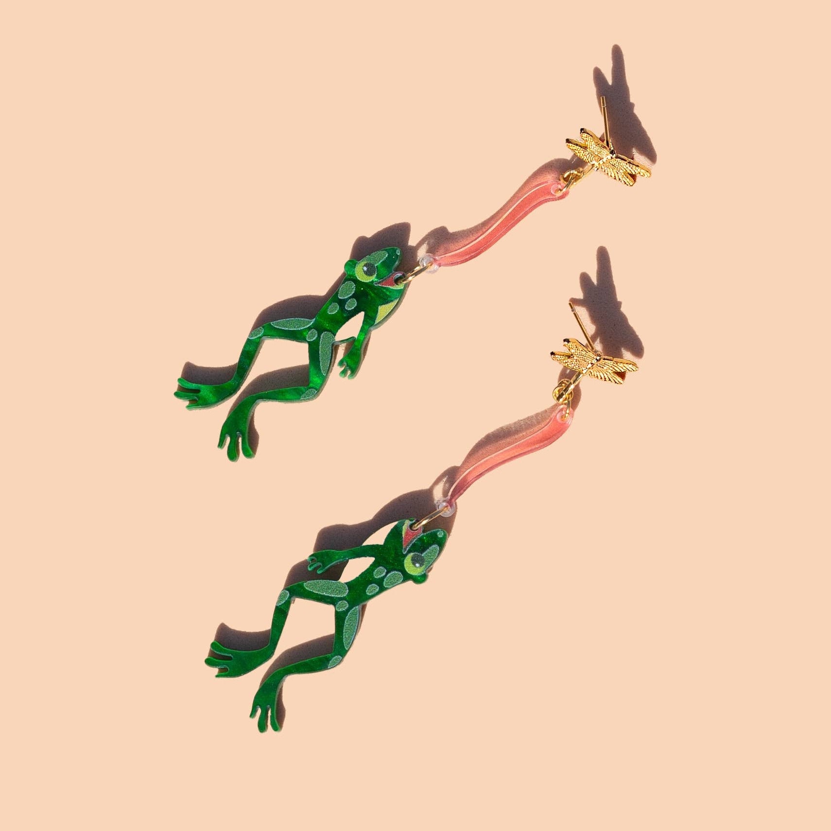 Pair of green and gold earrings on a beige background