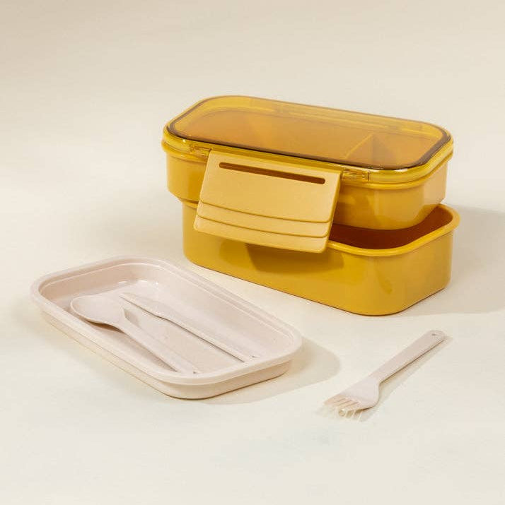 Yellow food storage container with a smaller container and utensils on a light background