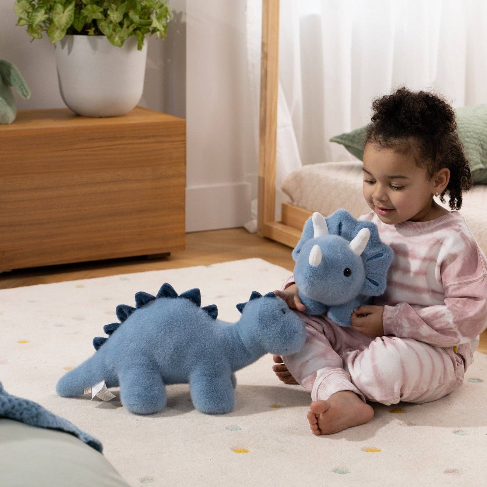 Child playing with blue dinosaur toys on a light-colored floor.