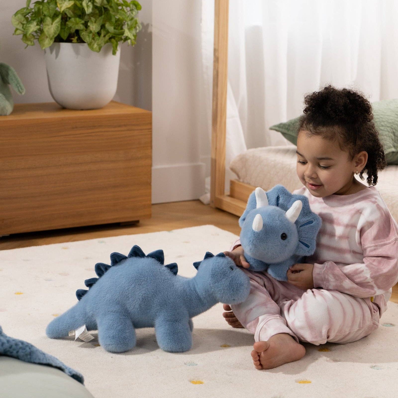 Child playing with blue dinosaur toys on a light-colored floor.