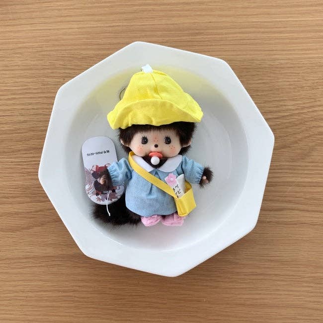 Toy monkey with a yellow hat and blue coat in a white bowl on a wooden surface