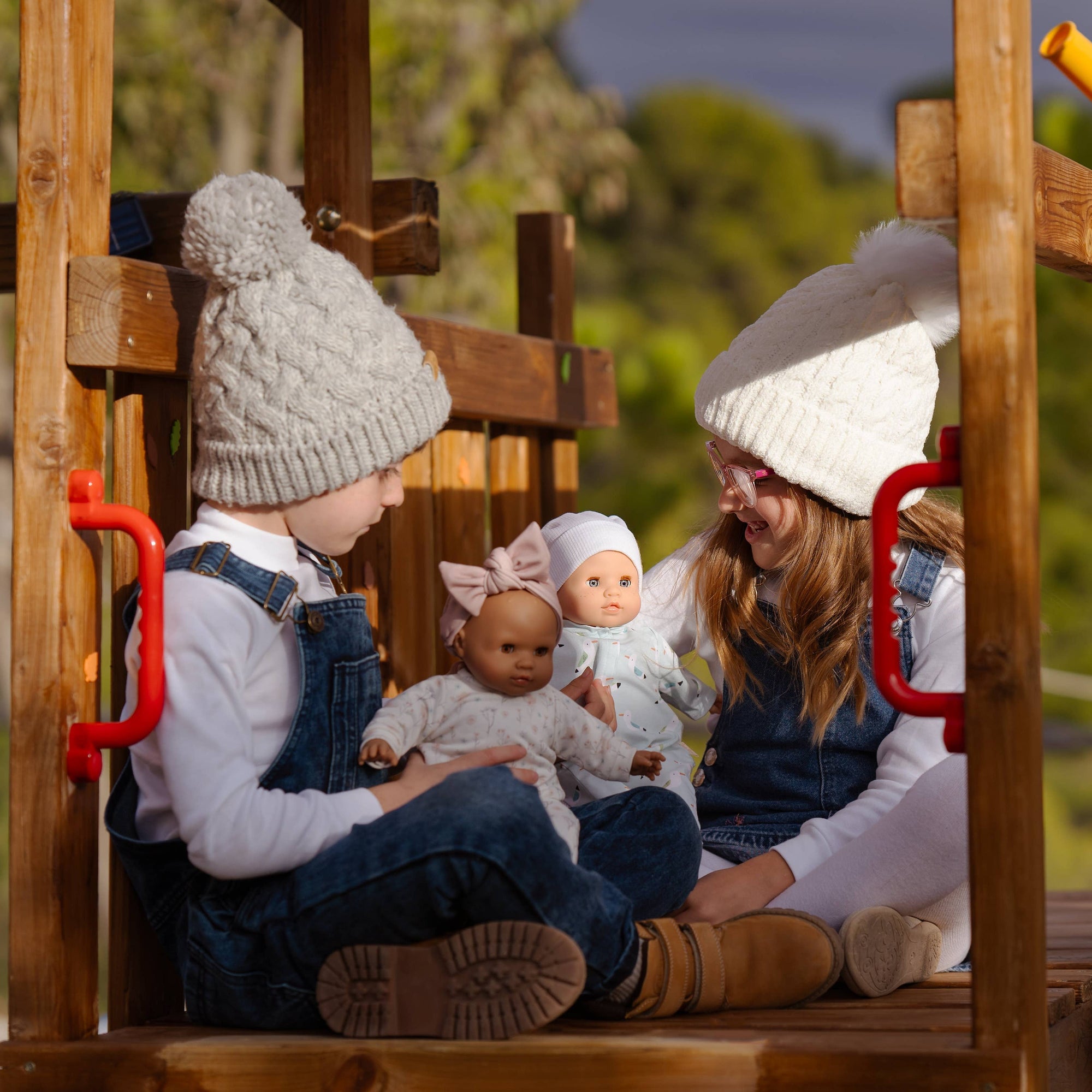 Two children playing with dolls on a wooden playground structure.