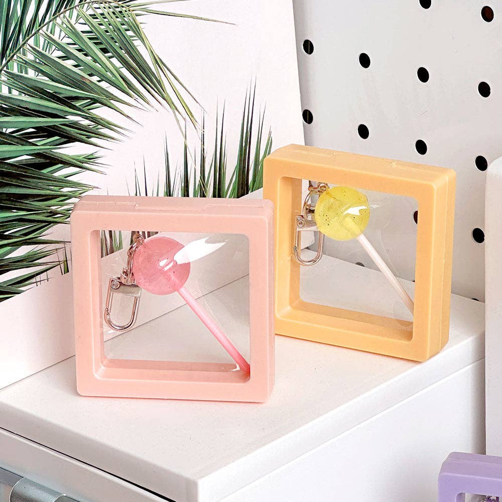 Two colorful square frames with lollipops on a white surface with a plant in the background