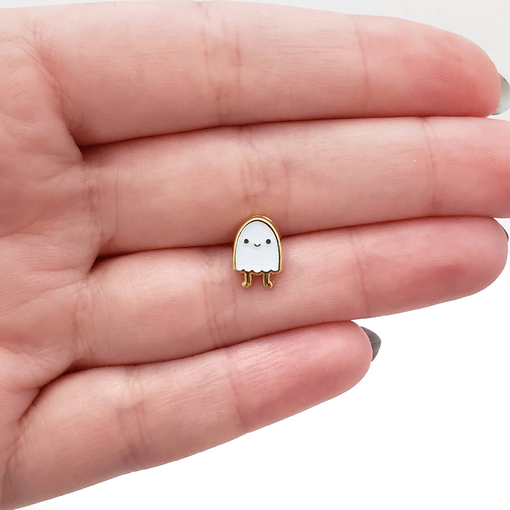 Small white ghost-shaped charm with a smiling face held between fingers on a light skin background