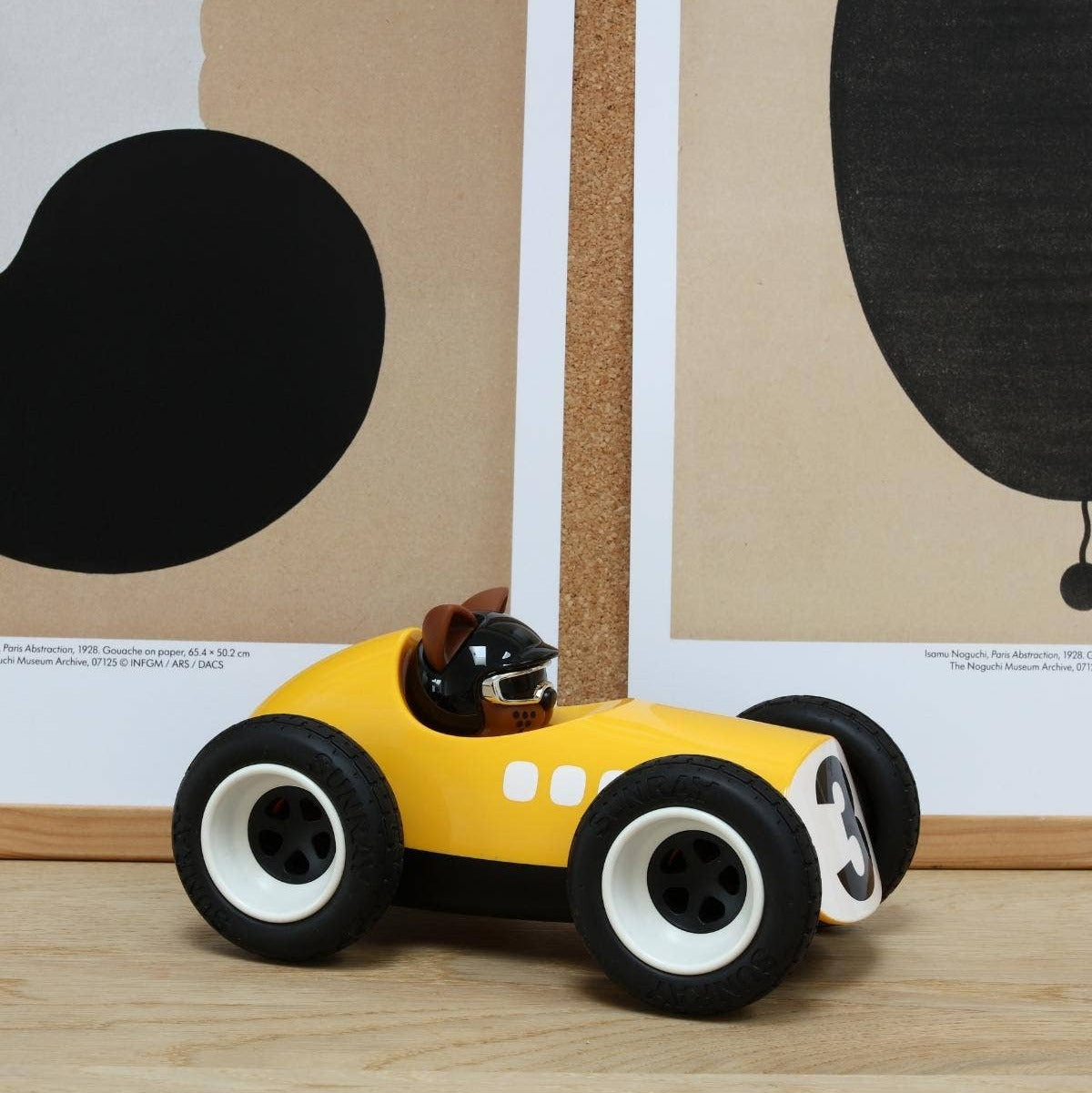 Yellow toy race car with a small figure inside on a wooden surface.