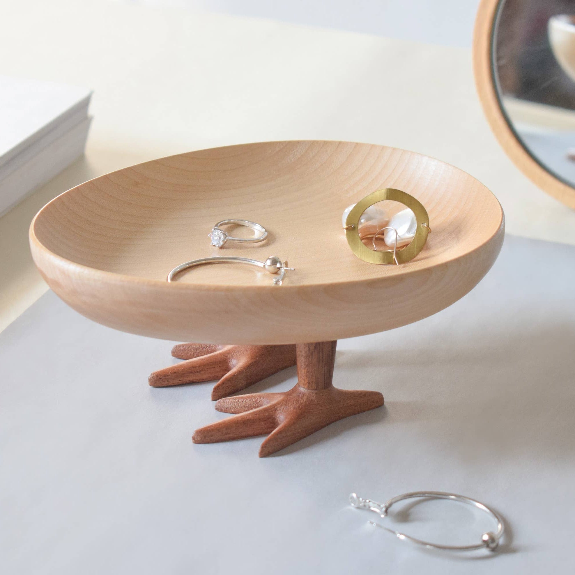 Wooden jewelry stand with small feet holding a ring, on a light surface.