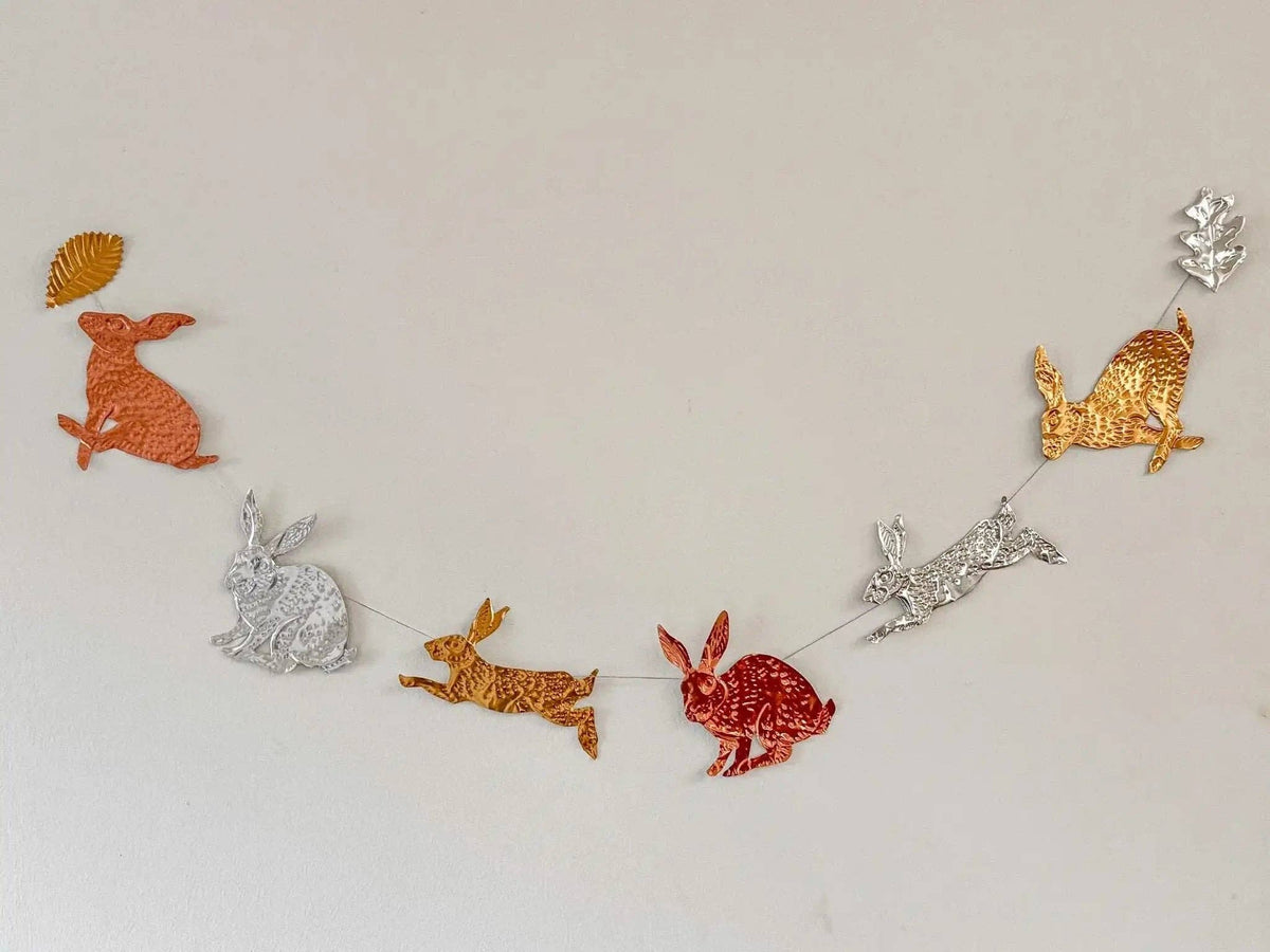A decorative garland made of metallic rabbit cutouts in orange, silver, gold, and red, strung across a plain light background.
