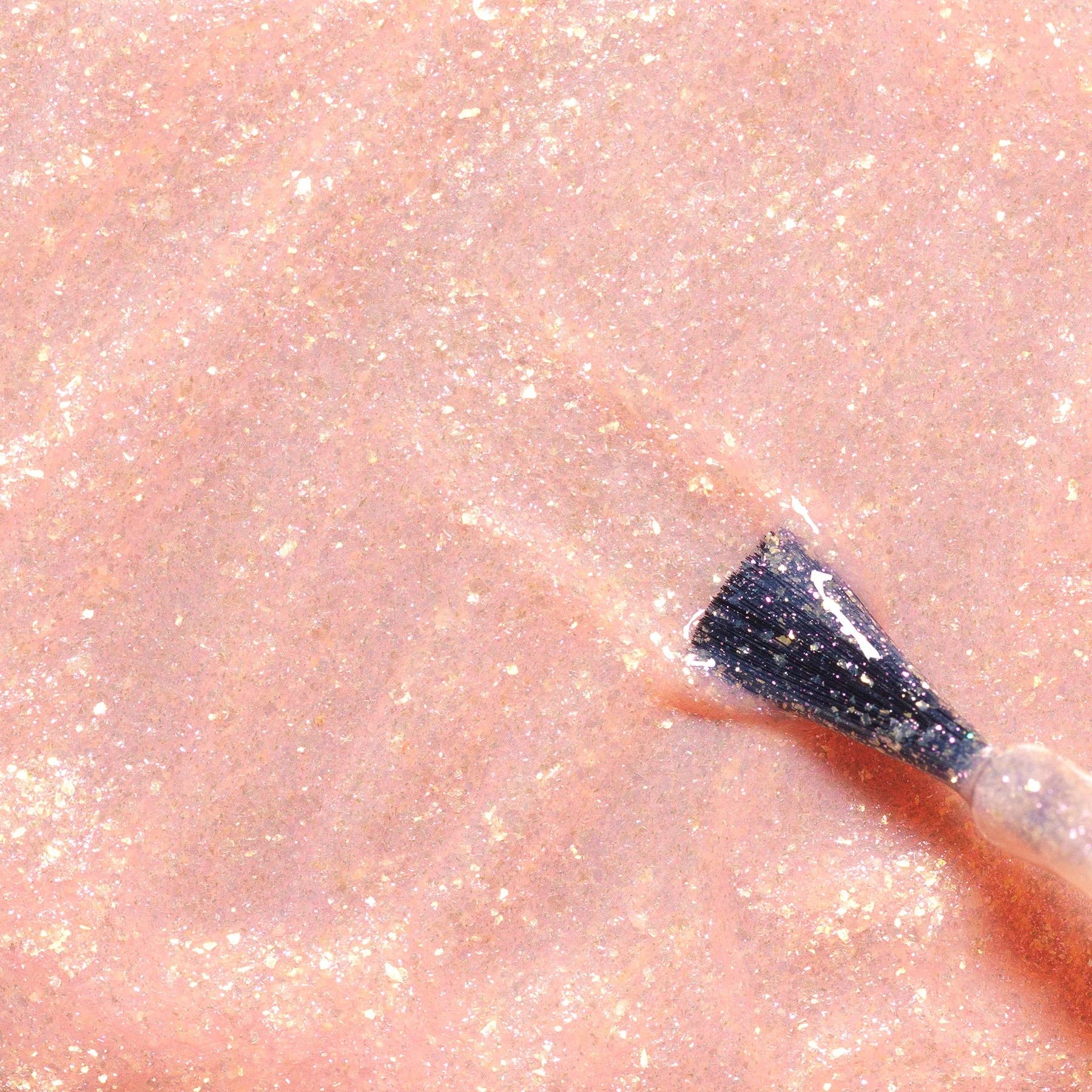 Close-up of glittery skin with a black applicator on a pink background