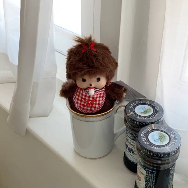 Stuffed monkey toy in a mug with jars of jam on a white surface