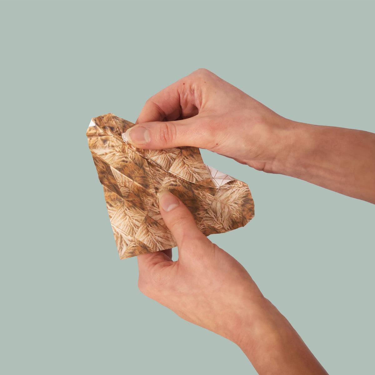 Hand holding a piece of gold leaf against a light green background