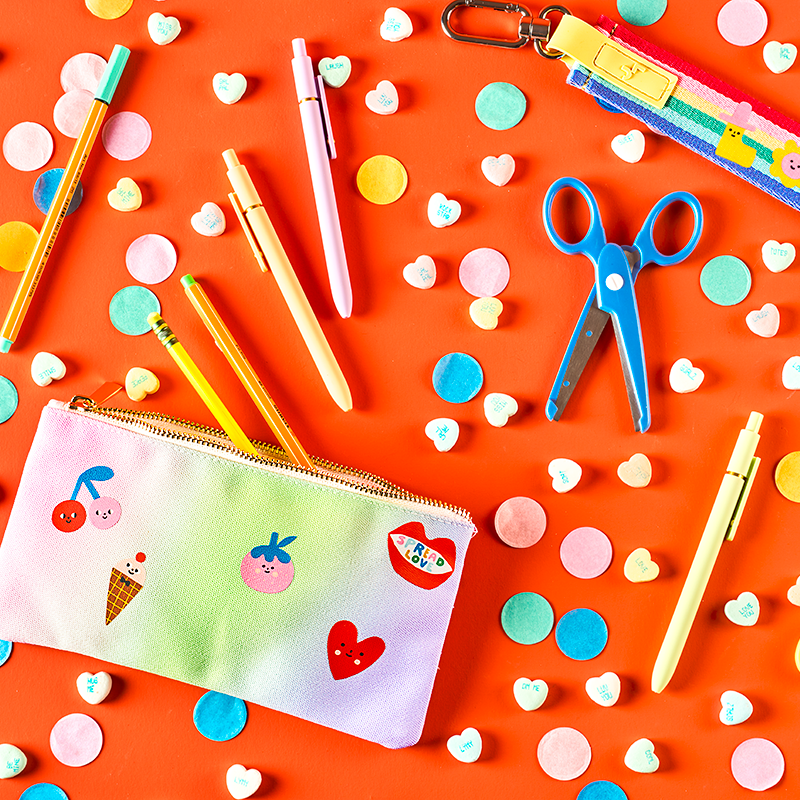 Colorful stationery items including pens, scissors, and a pencil case on a bright orange background with polka dots.