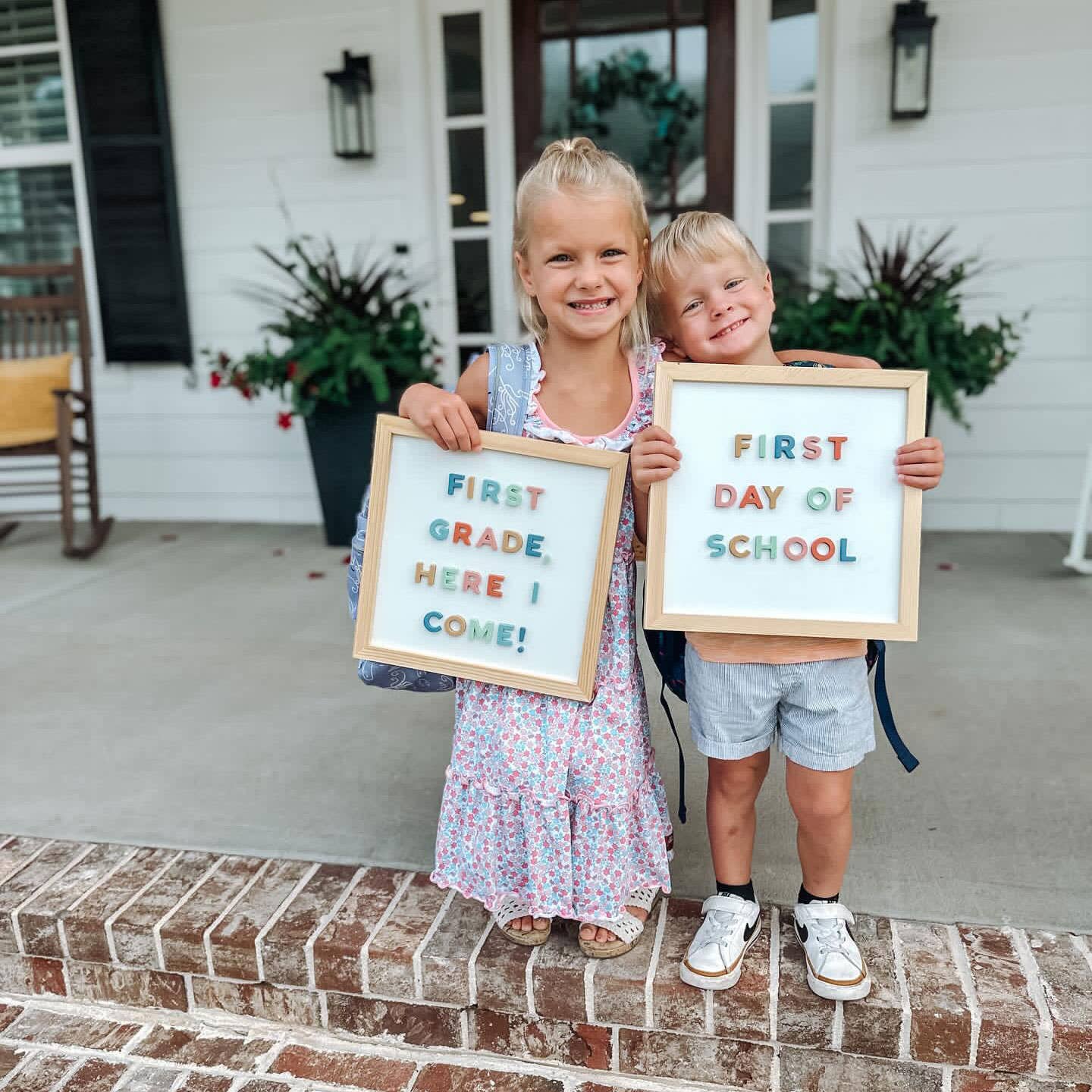 Two children holding signs for their first day of school on a front porch.