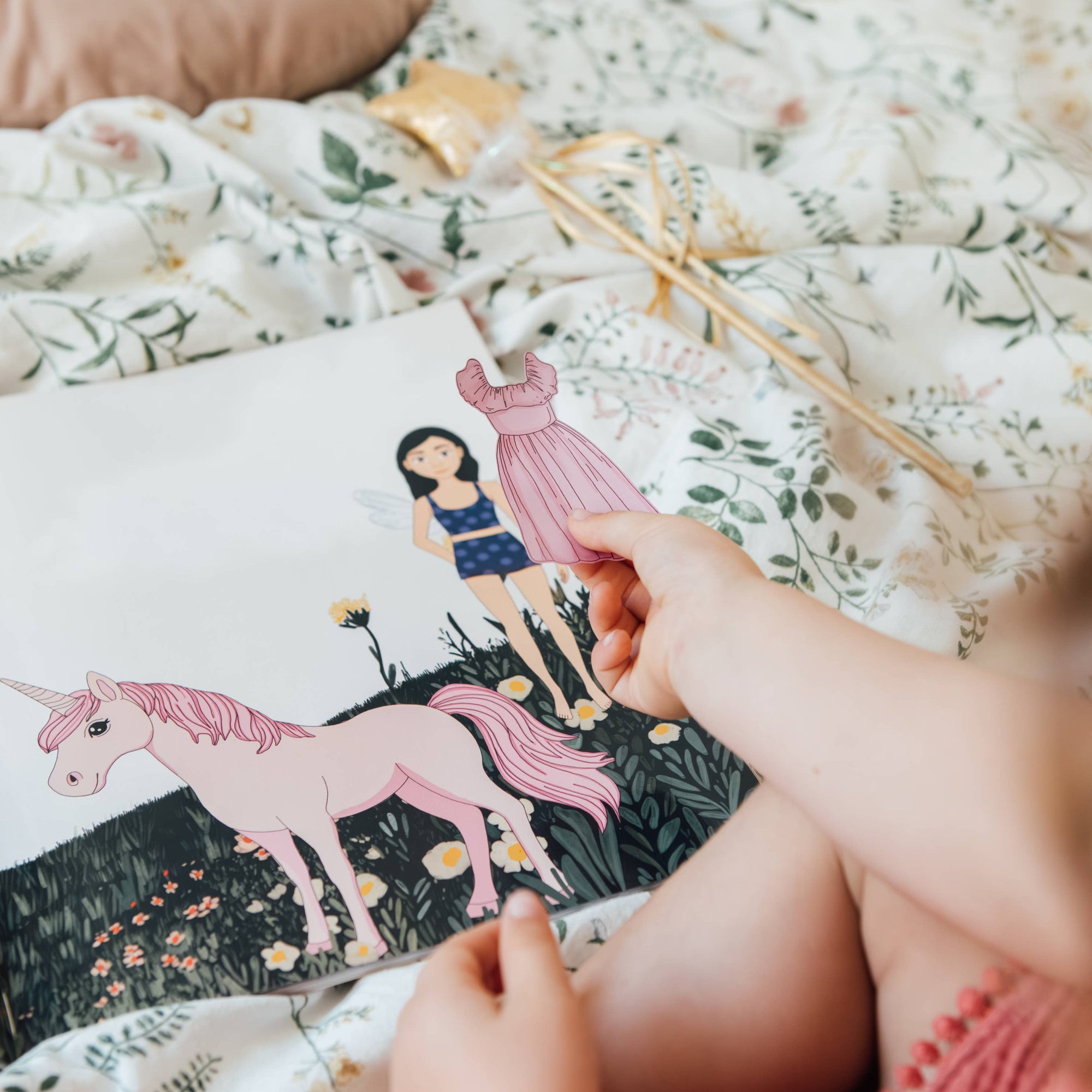 Person holding a book with a unicorn illustration on a floral bedspread