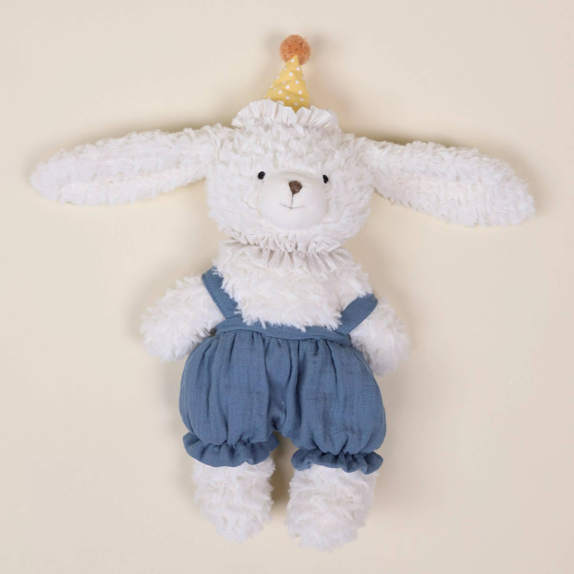 Stuffed toy rabbit with blue overalls on a beige background