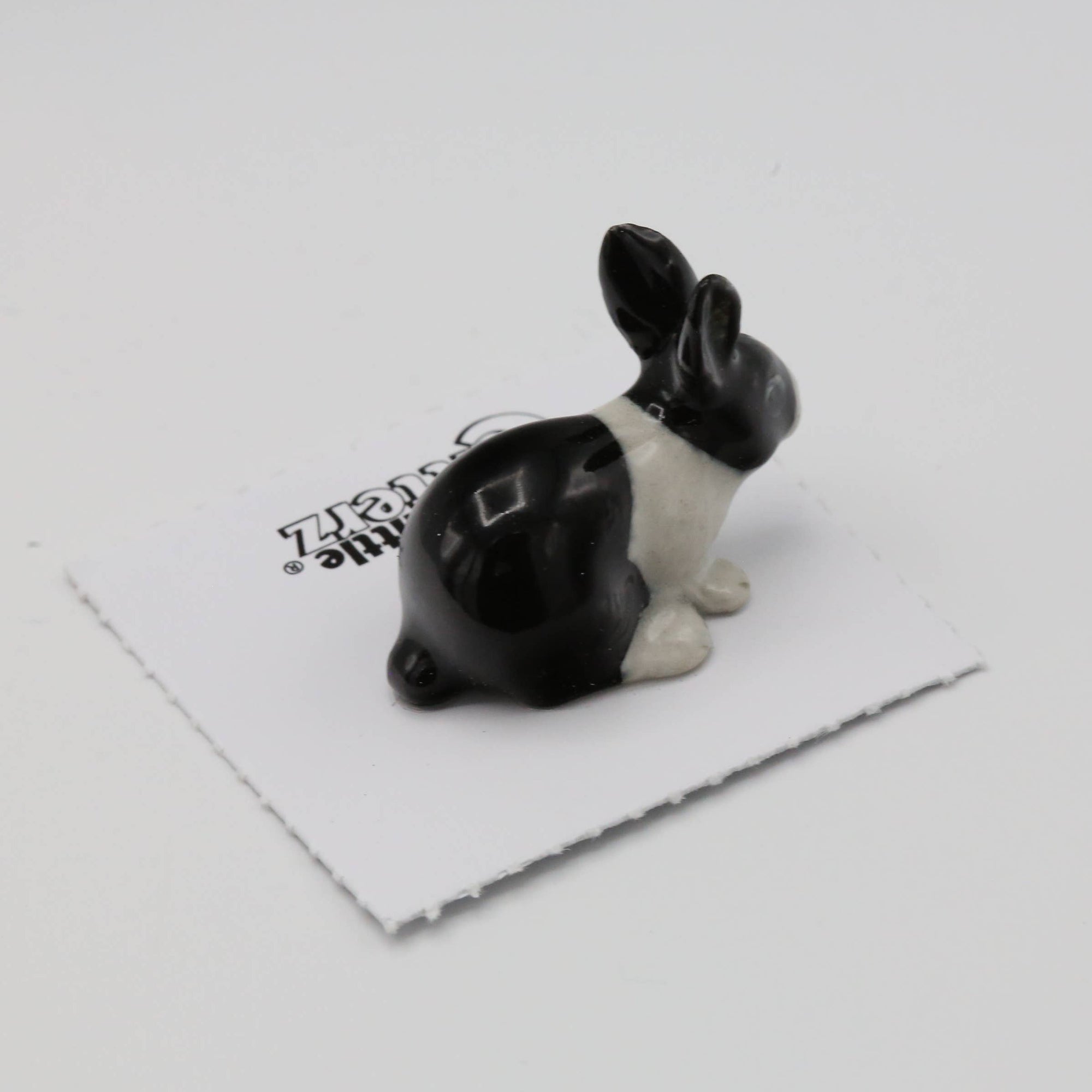 Black and white rabbit figurine on a white surface with a brand logo in the background.