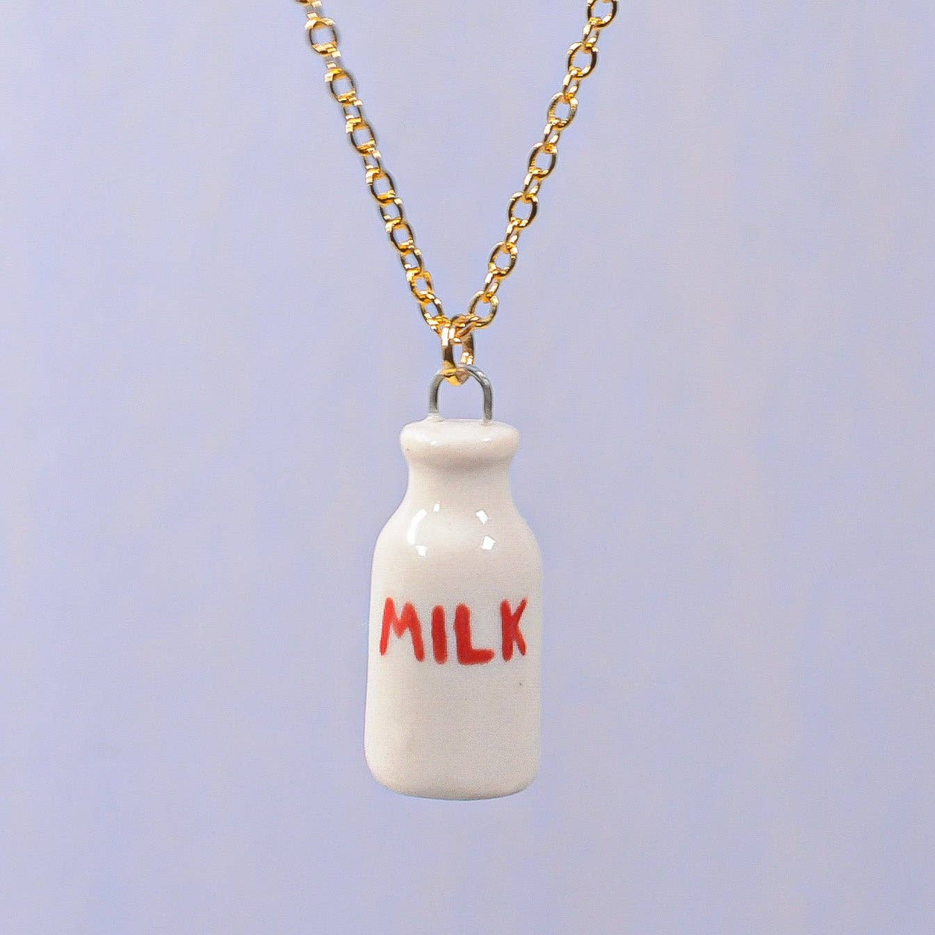 Miniature white milk bottle pendant with 'MILK' text on a gold chain against a light blue background