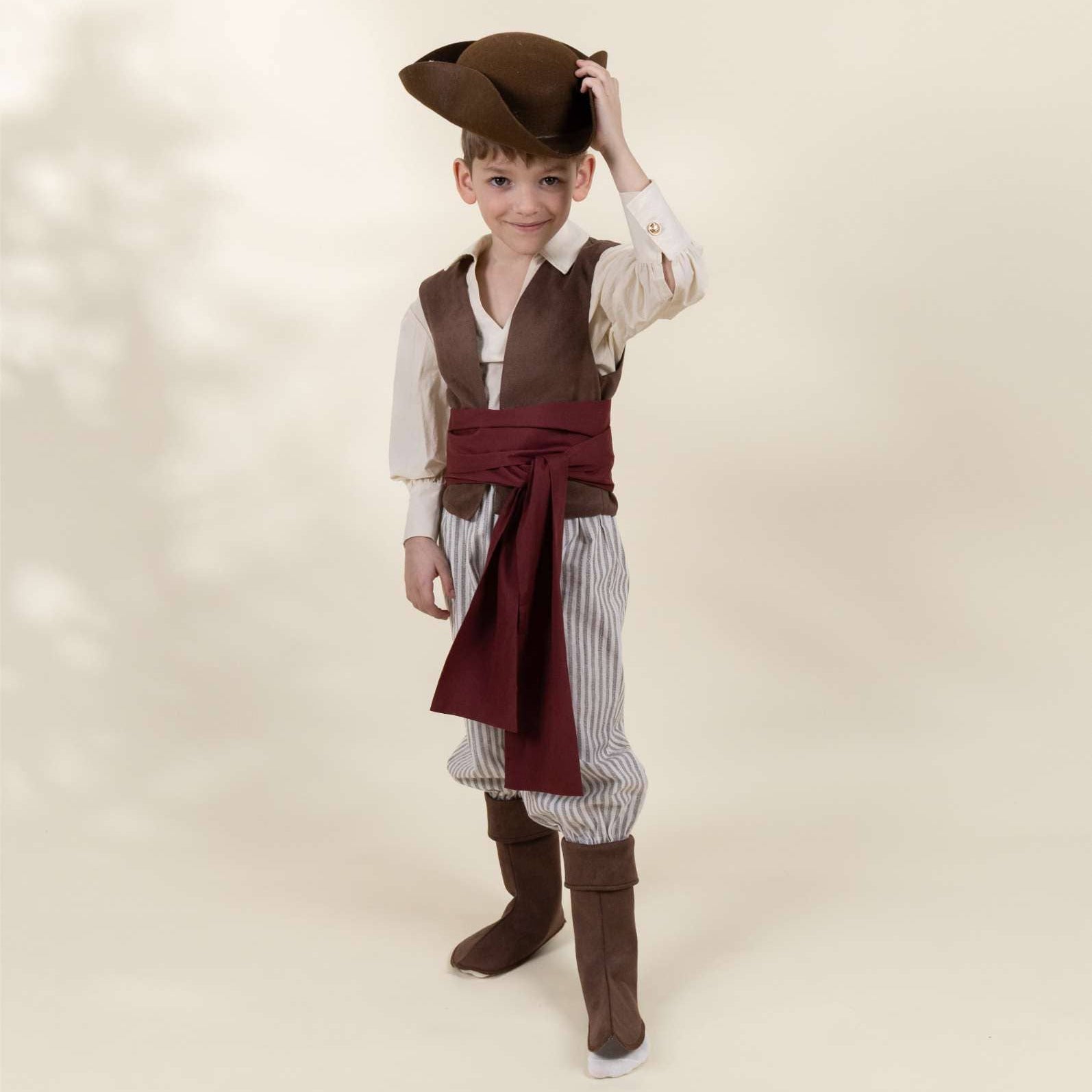 Child wearing a historical costume with a vest, shirt, pants, and hat on a light background