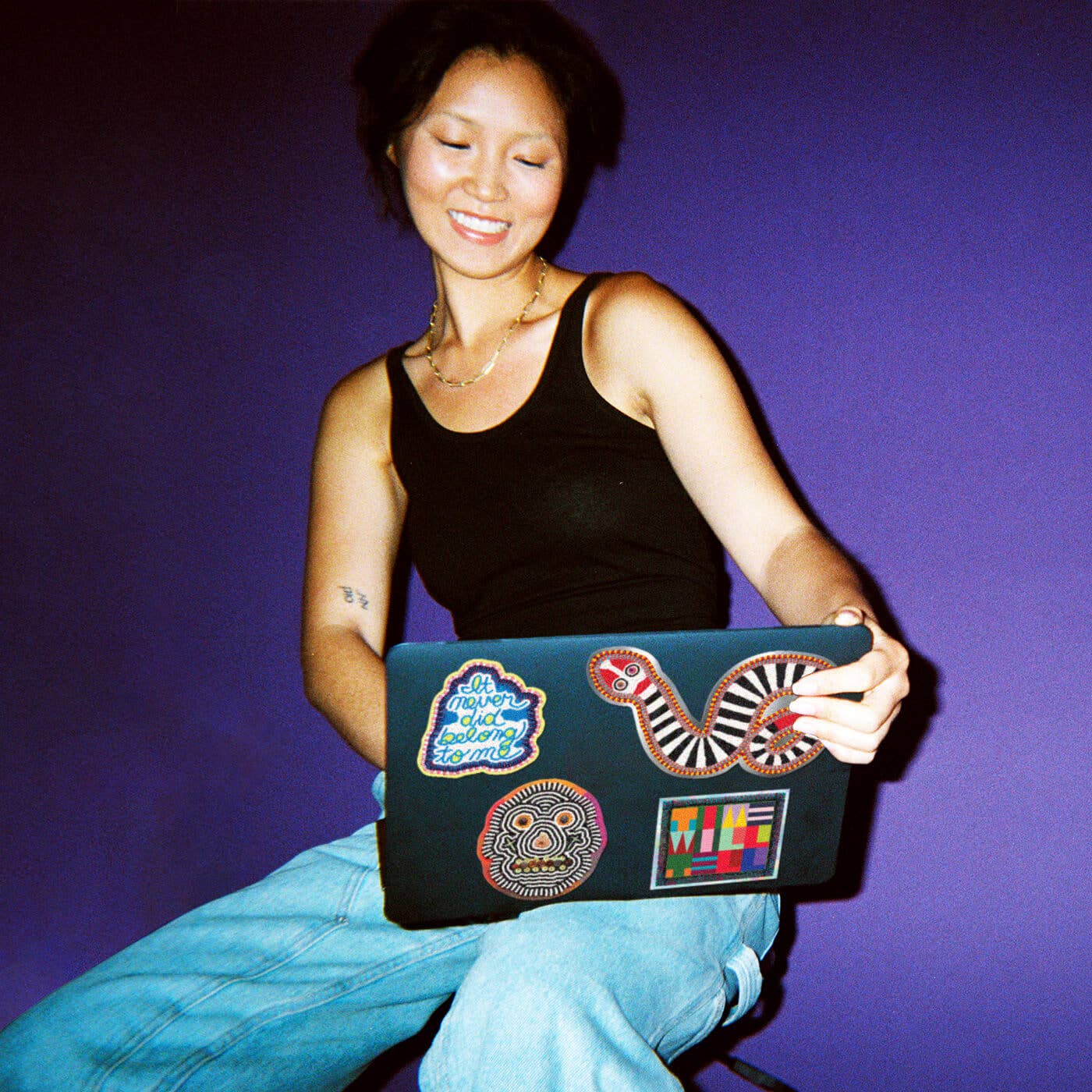 Person holding a laptop with colorful stickers against a purple background