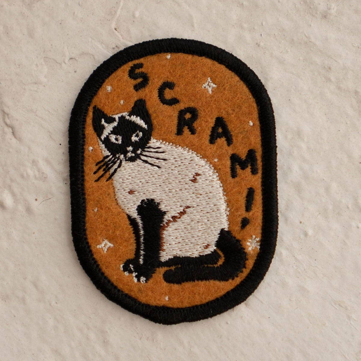 Embroidered patch with a cat illustration and 'SCRAM!' text on a textured beige background