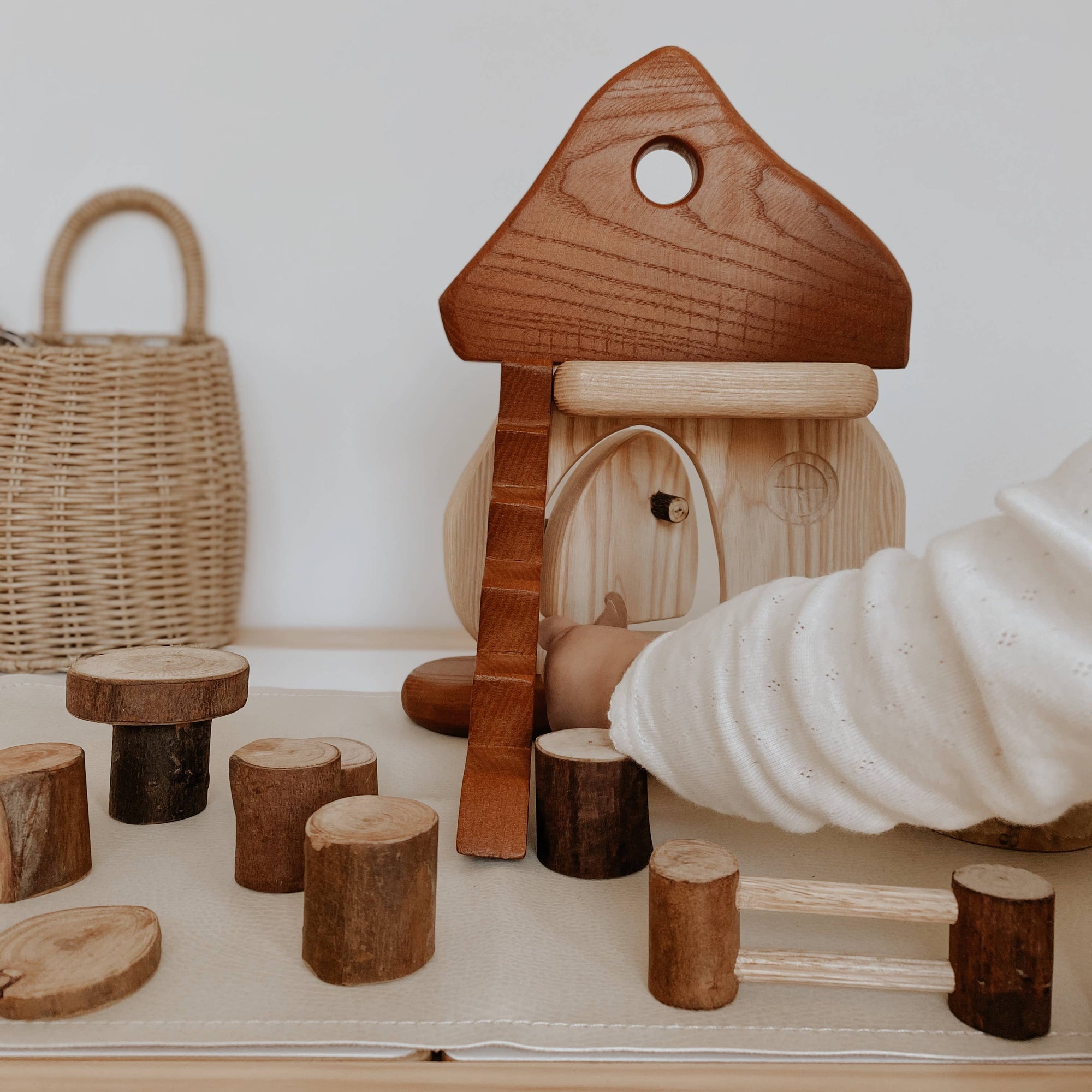 Wooden toy house with a child's hand reaching towards it on a light surface.