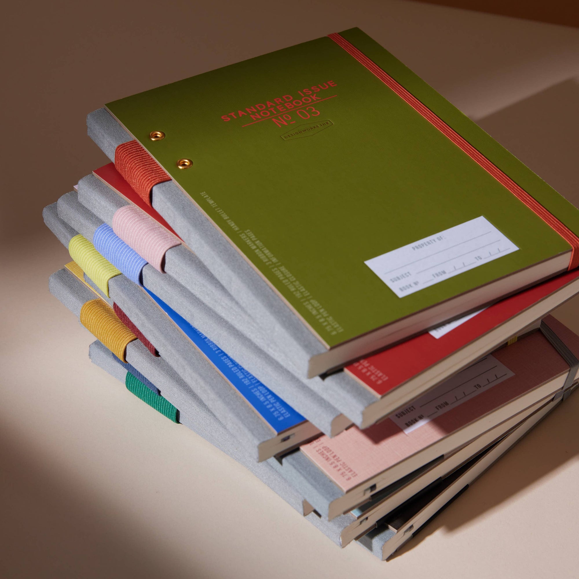 Stack of colorful notebooks on a beige surface with a warm light.