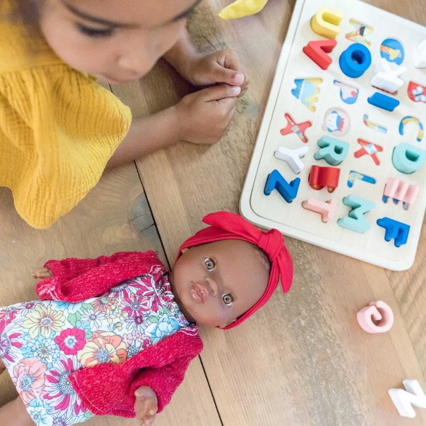 Child playing with a doll and alphabet puzzle on a wooden floor