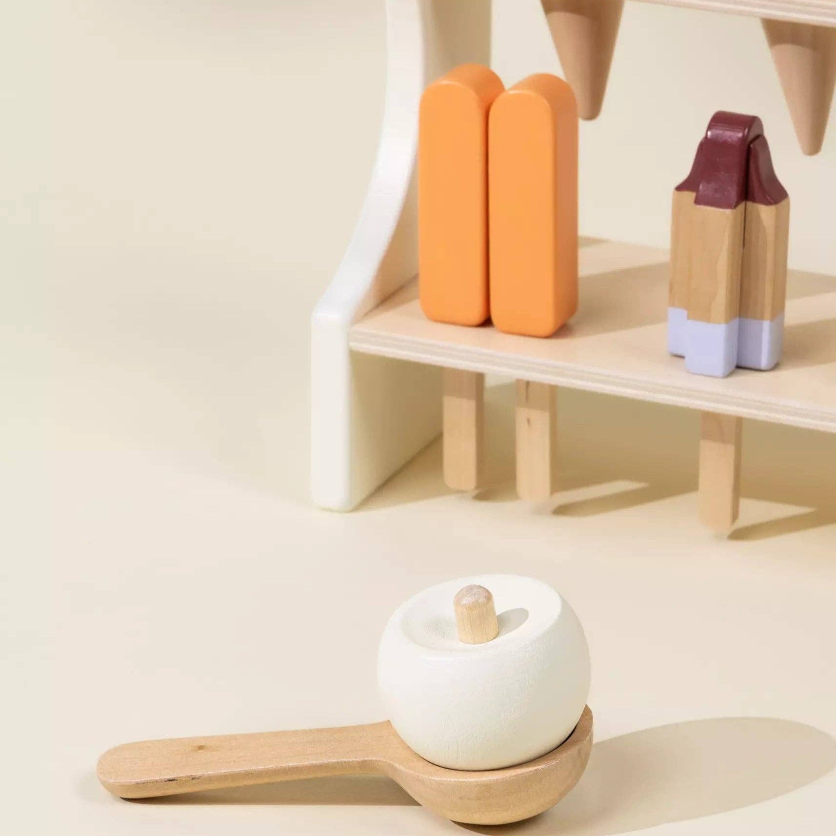 Wooden toy set with a white apple, orange popsicles, and purple container on a beige shelf.