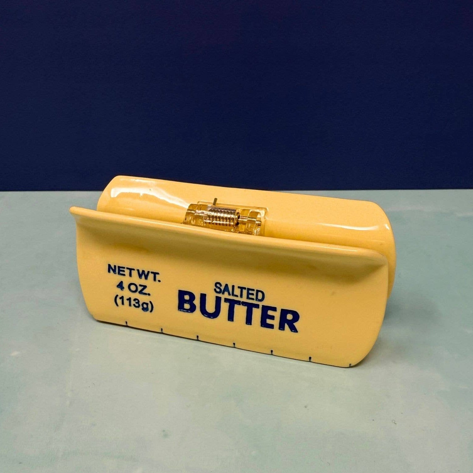 Yellow butter container with blue text on a gray surface and dark blue background