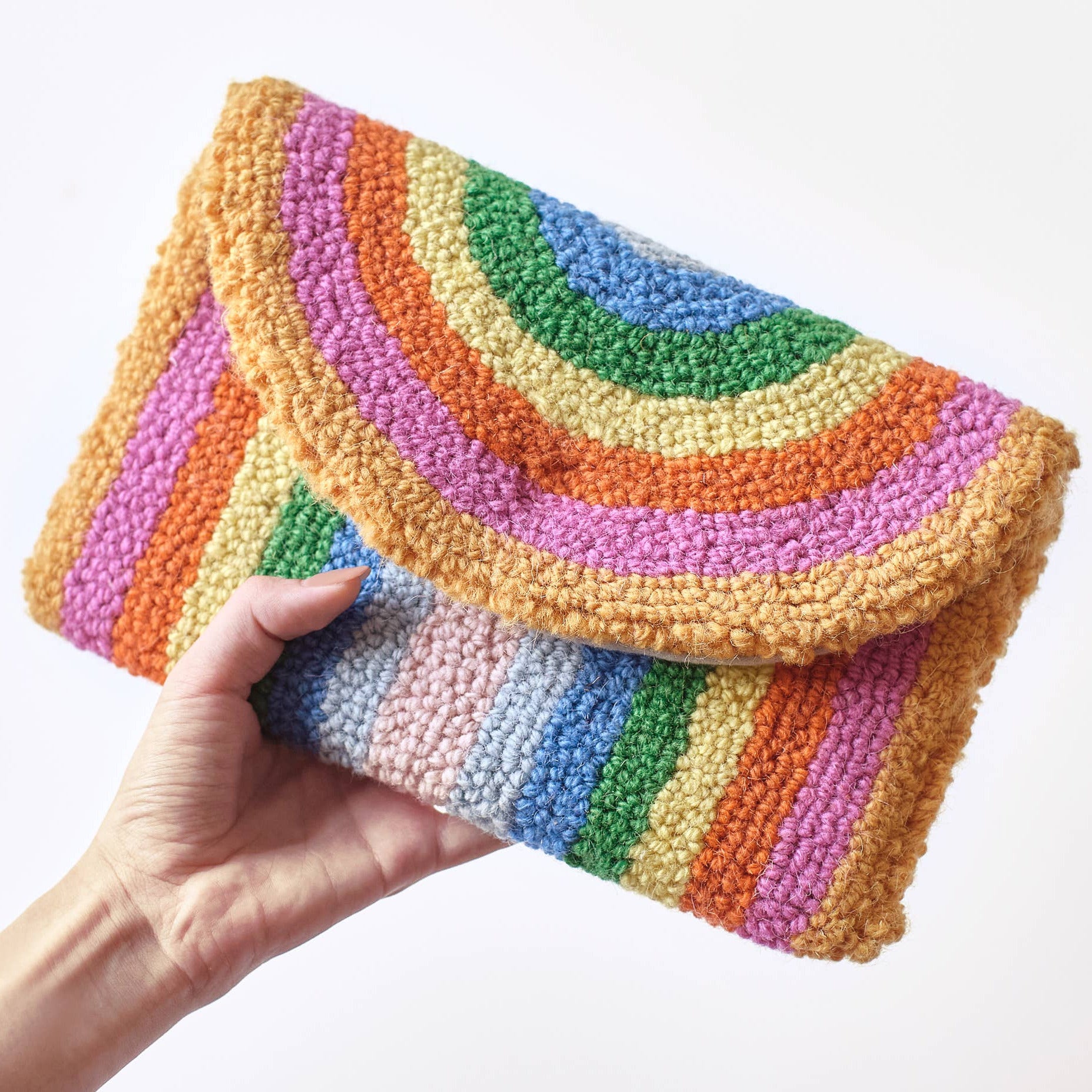 Hand holding a colorful striped clutch against a white background