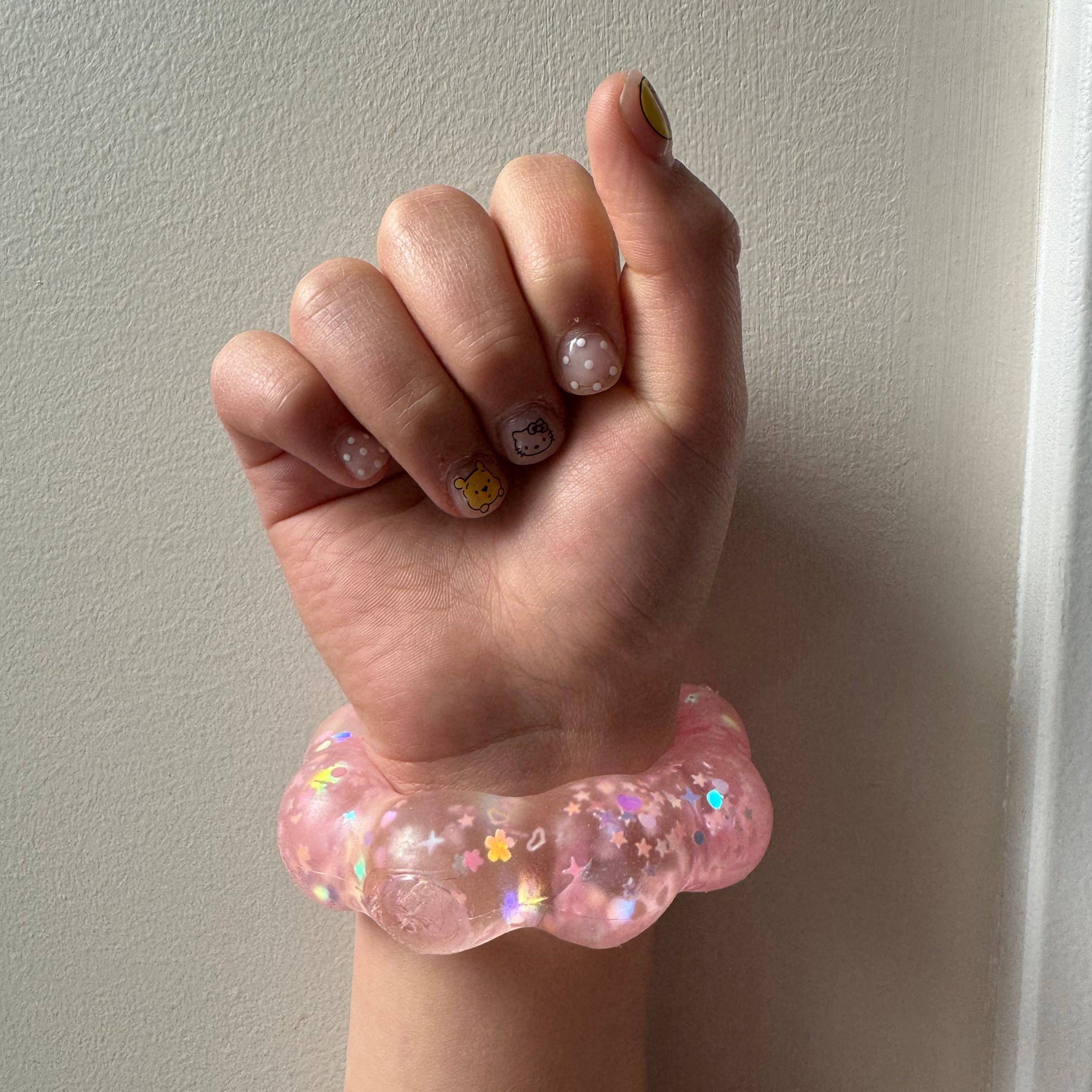 Hand wearing a pink glittery bracelet against a plain background