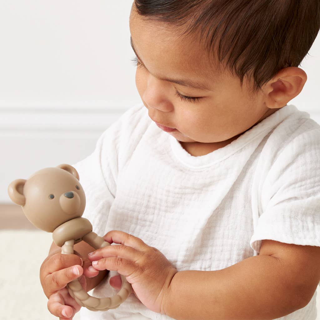 Baby holding a teddy bear-shaped teething toy against a white background