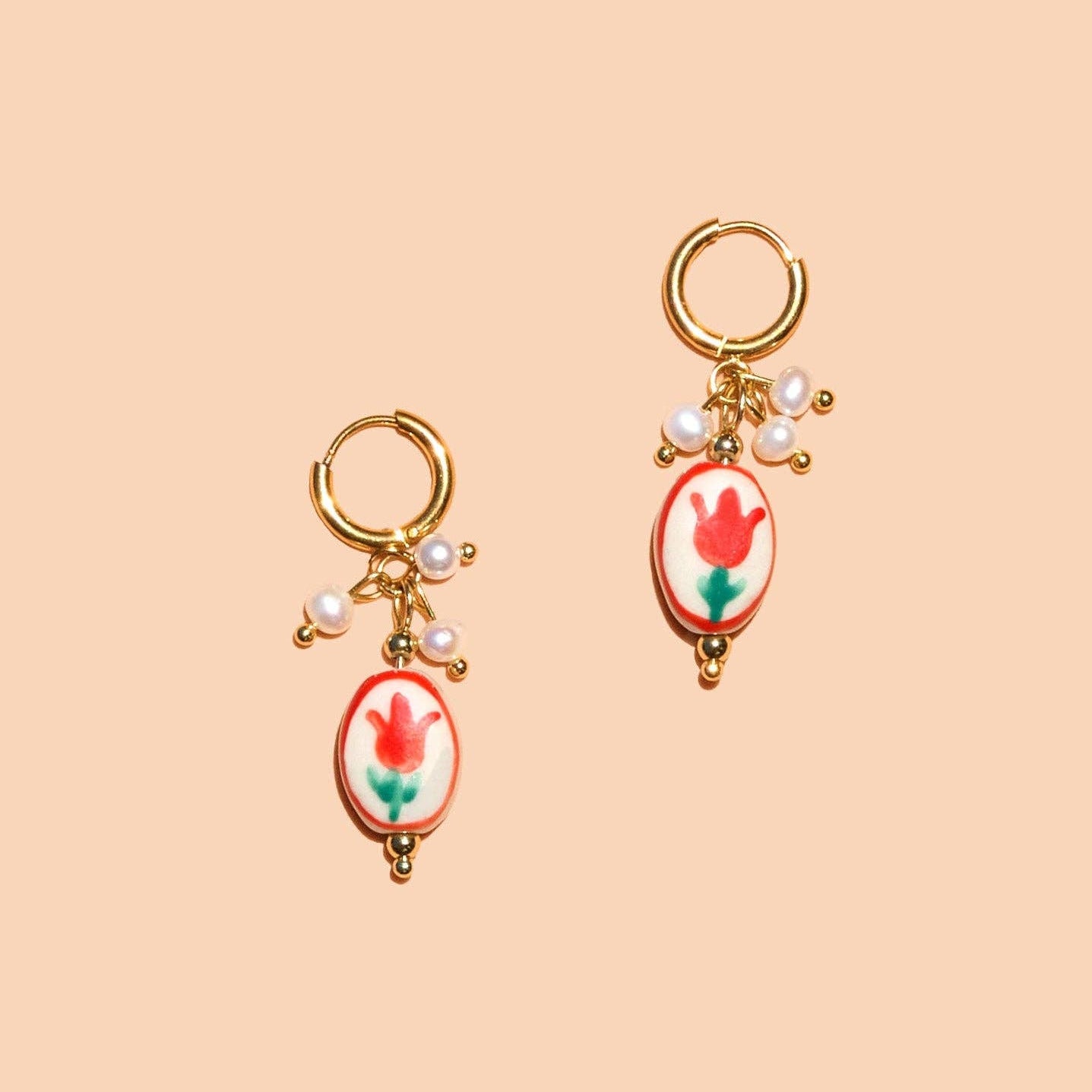 Pair of gold earrings with floral designs on a beige background