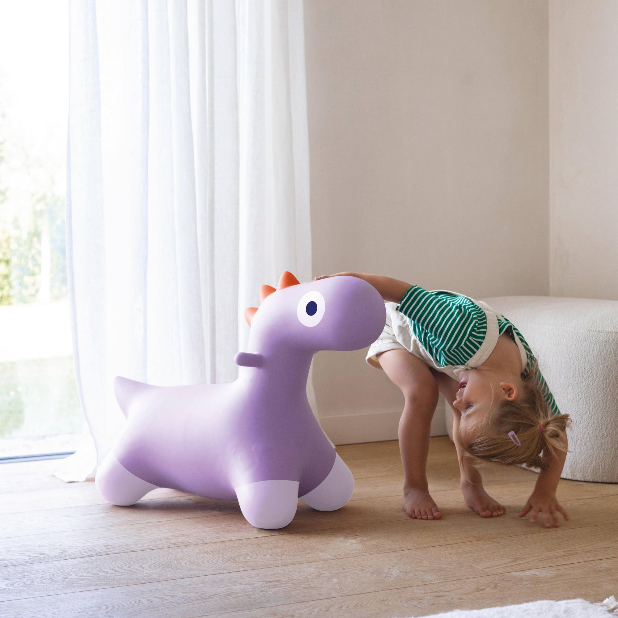 Child playing with a purple inflatable unicorn toy in a bright room.