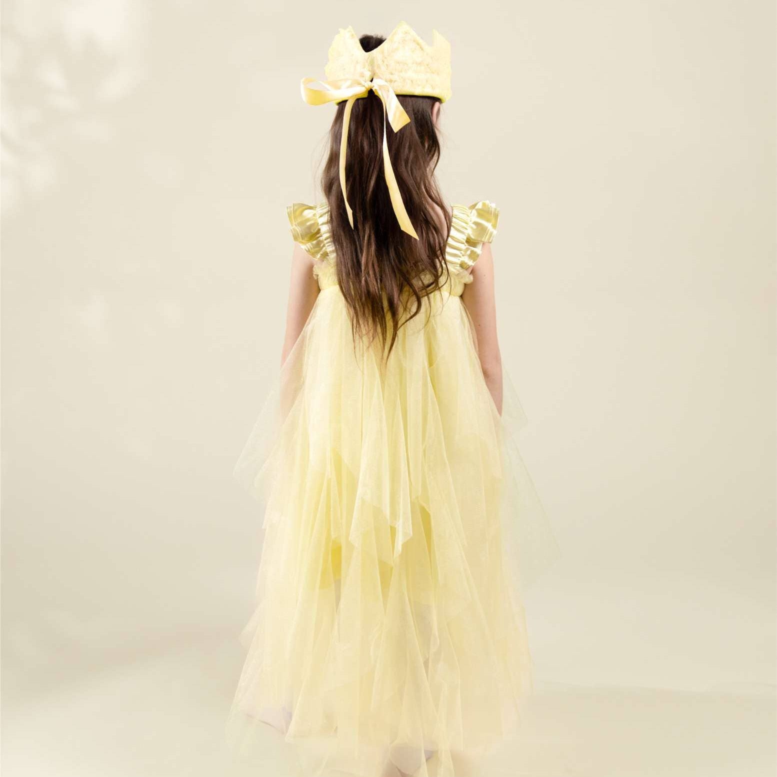 Young girl wearing a yellow dress with a large bow on her head against a light background