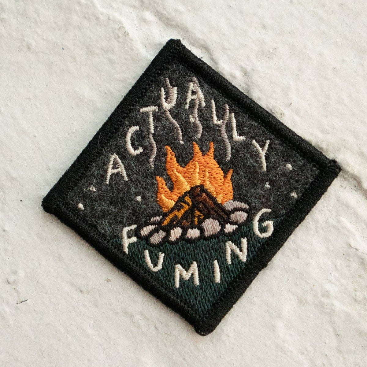 Embroidered patch with a campfire design and text on a textured white background