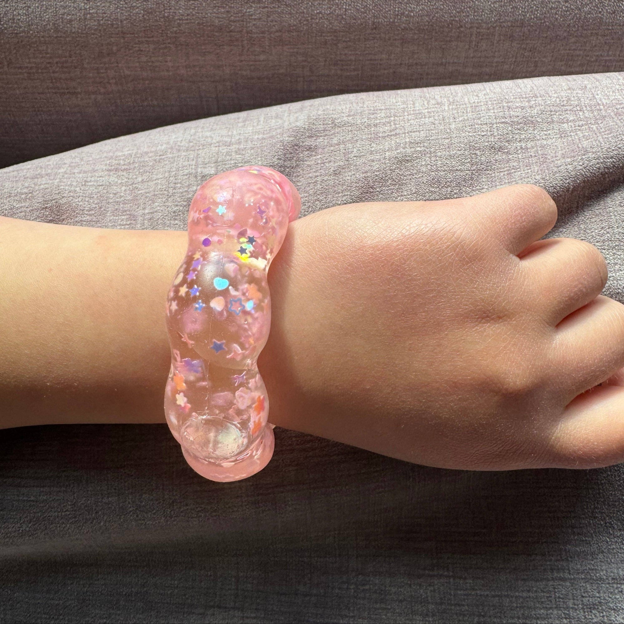 Pink glittery bracelet on a child's wrist against a gray background