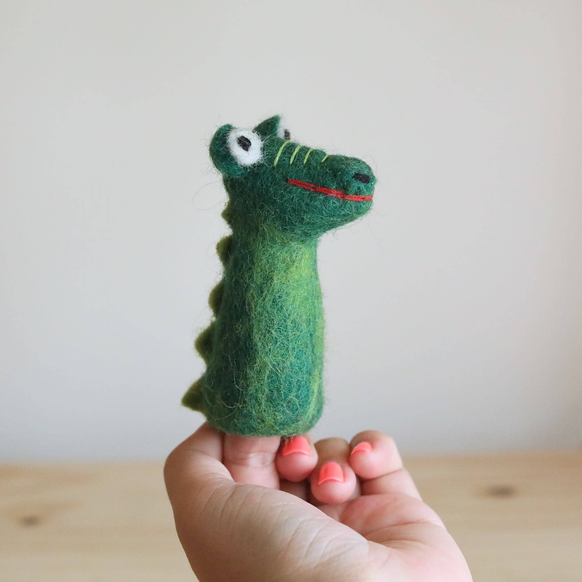 Hand holding a green crocodile-shaped toy against a plain background