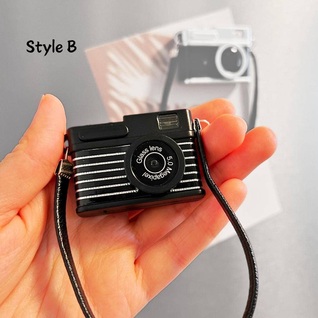 Small black camera with a strap held in a hand, with a blurred background