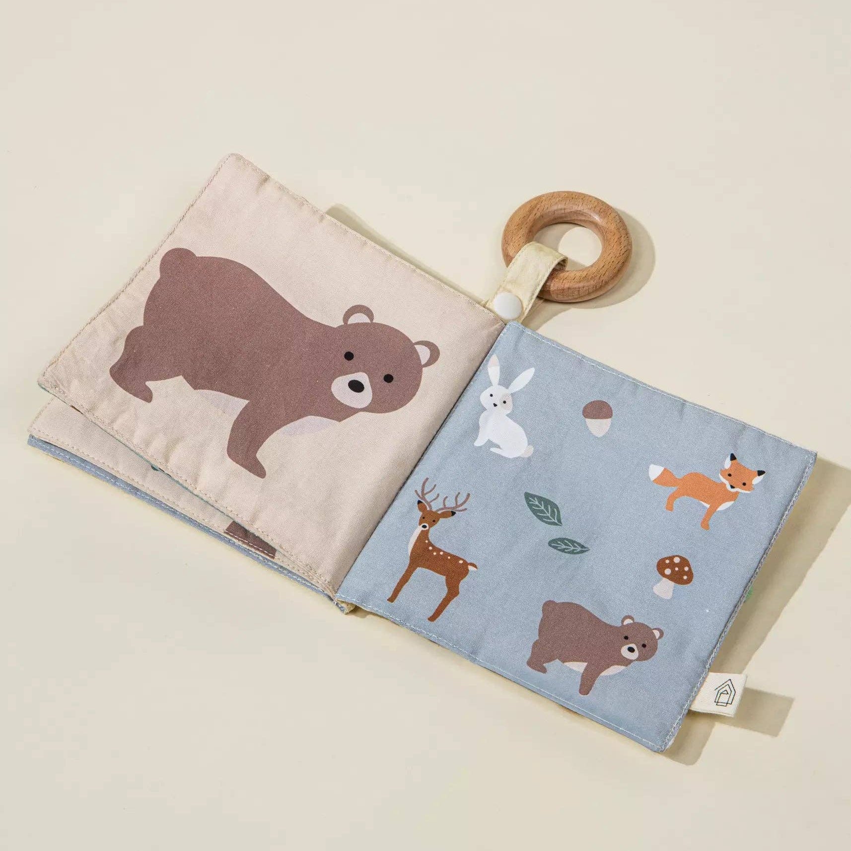 Baby book with wooden ring and animal illustrations on a beige background