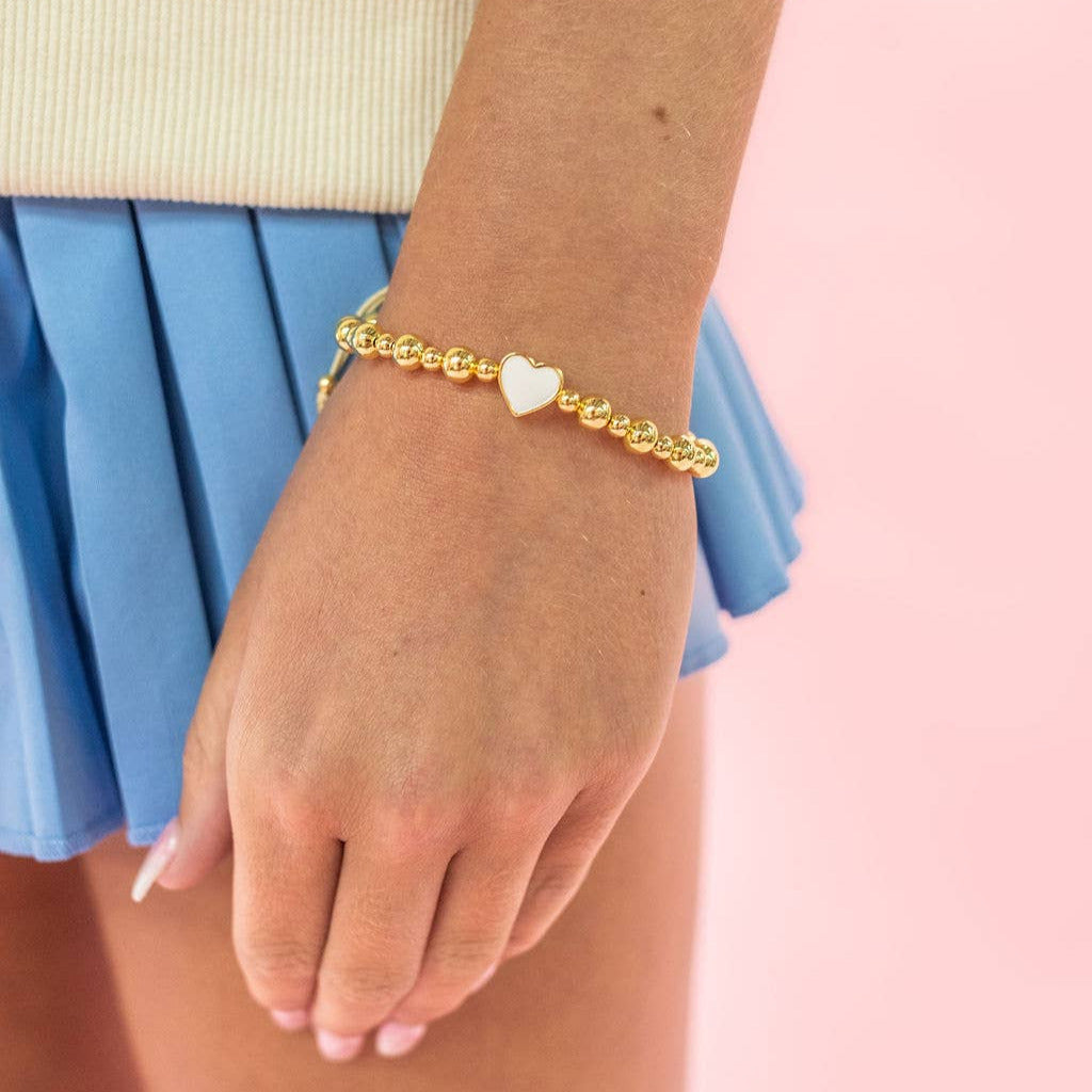 Gold bracelet with a heart charm on a wrist against a pink background