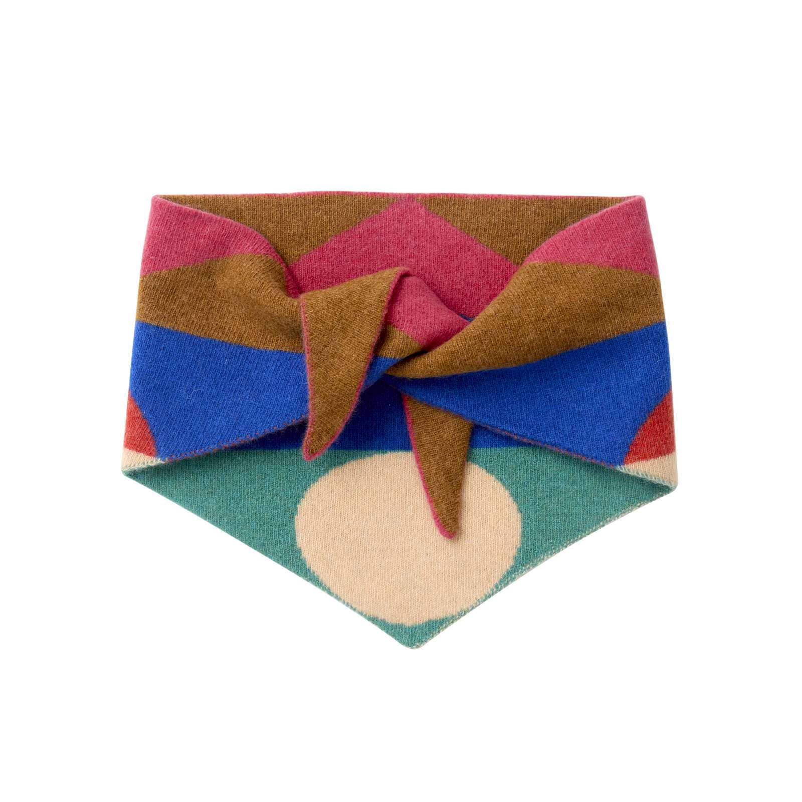 A multicolor patterned pet bandana featuring a large knot, with geometric stripes of brown, pink, blue, teal, and cream, and a large cream circle at the pointed bottom.