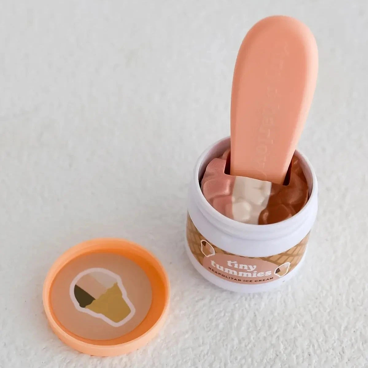 Small container of doll food with a pink spoon on a light gray background