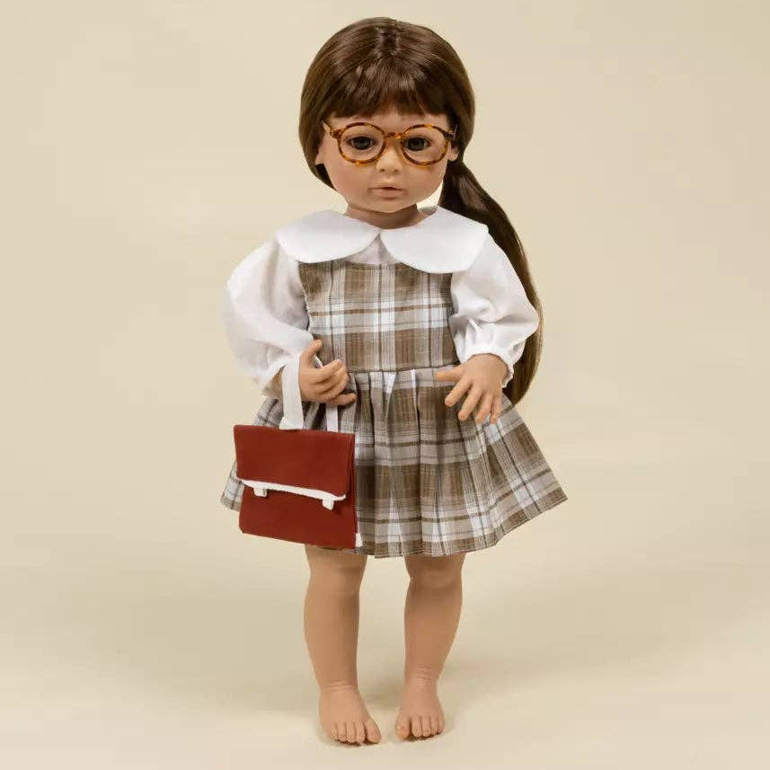 Doll wearing a plaid dress and holding a red book against a beige background