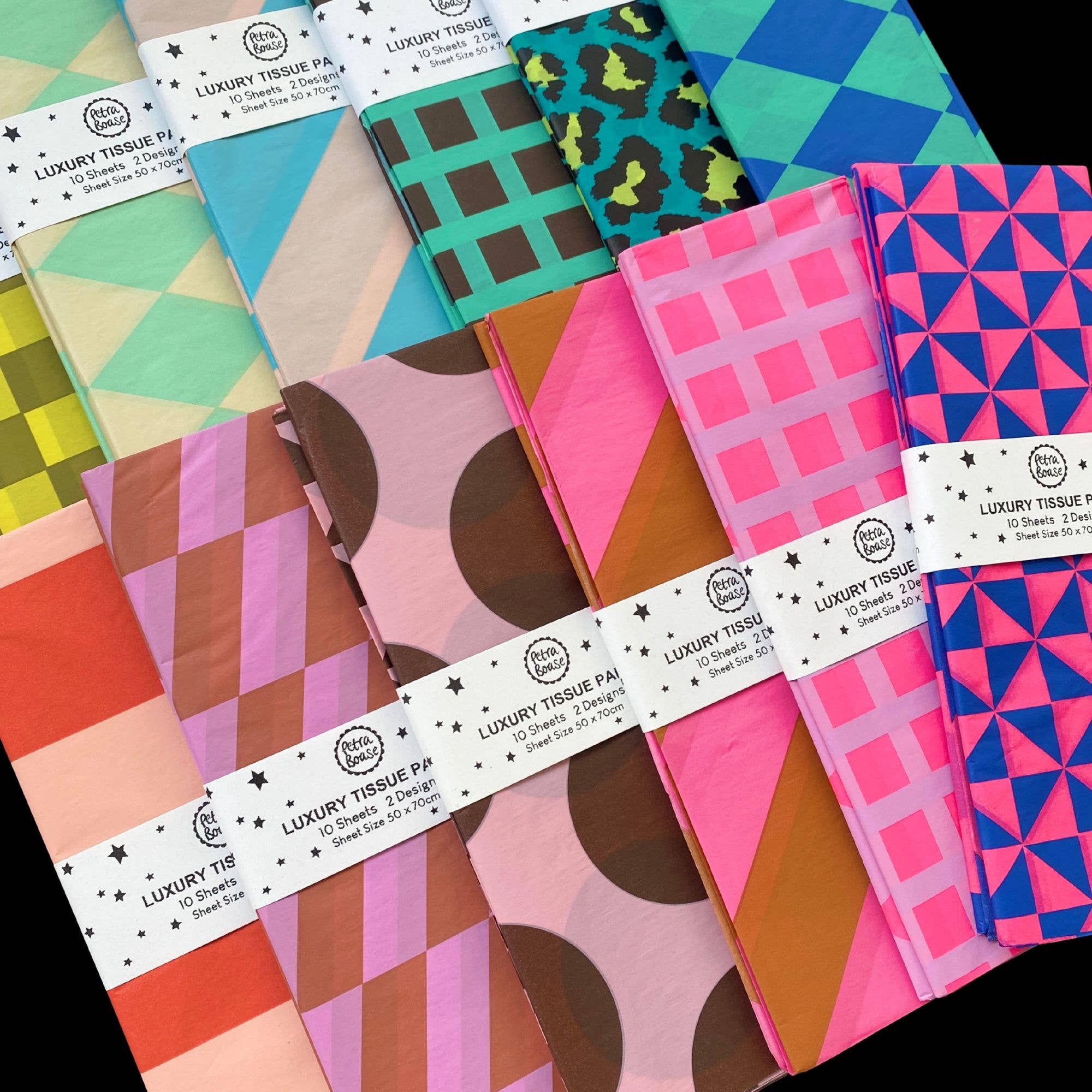 A set of folded luxury tissue paper packs arranged in a fan shape, showcasing various colorful geometric and abstract patterns. The packs are wrapped in white paper bands labeled 'LUXURY TISSUE PAPER' with a circular 'The Paper Company' logo.